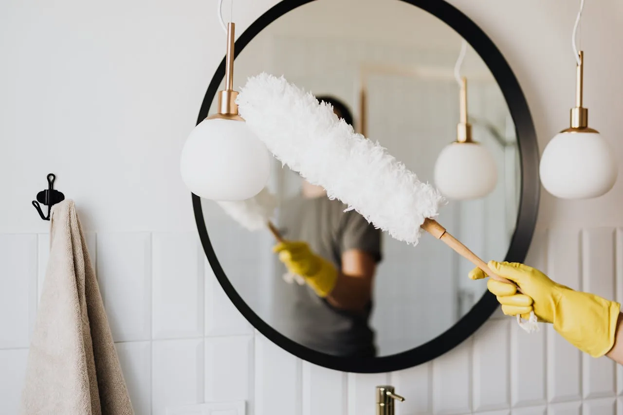 Home A person cleaning an elegant bathroom mirror with a fluffy duster and yellow gloves.