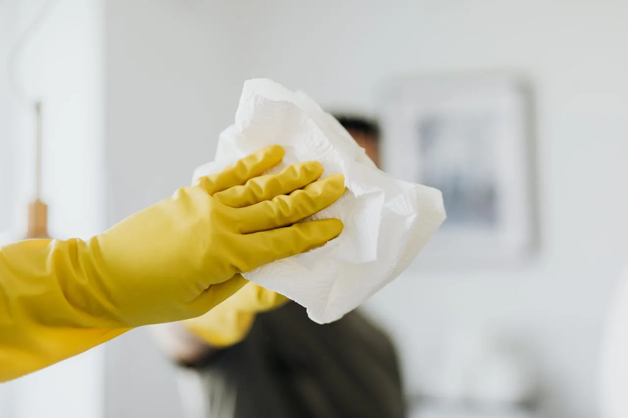 Services Close-up of a yellow-gloved hand cleaning a mirror with a cloth indoors.